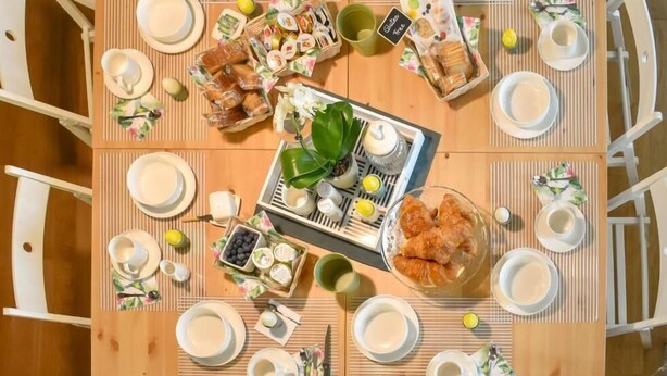 A breakfast setting with a variety of food items and drinks on a wooden table, surrounded by white chairs. - B&B VILLA ELISA (Motta di Livenza)