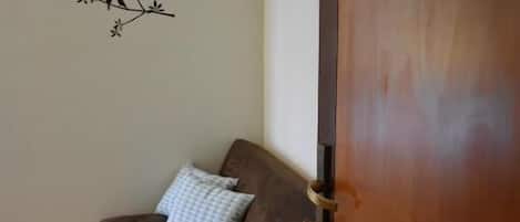 Una habitación con una puerta de madera, un sofá marrón con un cojín estampado y un adhesivo mural con aves en una rama.