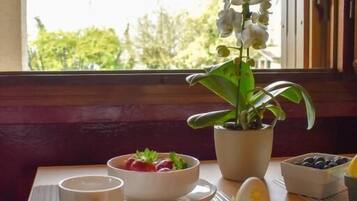 A breakfast table with a potted orchid, a bowl of strawberries, a cup, and a pitcher.