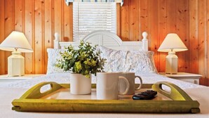 A wooden paneled room with a bed, two bedside lamps, a tray with a mug, a remote control, and a potted plant. - Cocktail Time-6Br/3.5BA in Ocean Drive-Pet Friendly (North Myrtle Beach)