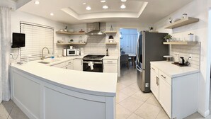 Une cuisine moderne dotée d’un îlot central, de meubles blancs, d’un four à micro-ondes encastré, d’une cuisinière et d’un réfrigérateur.