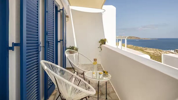 En balkong med vita stolar, ett litet bord och utsikt över havet.