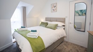 A neatly made bed with white and green linens, a headboard, and a painting above it.