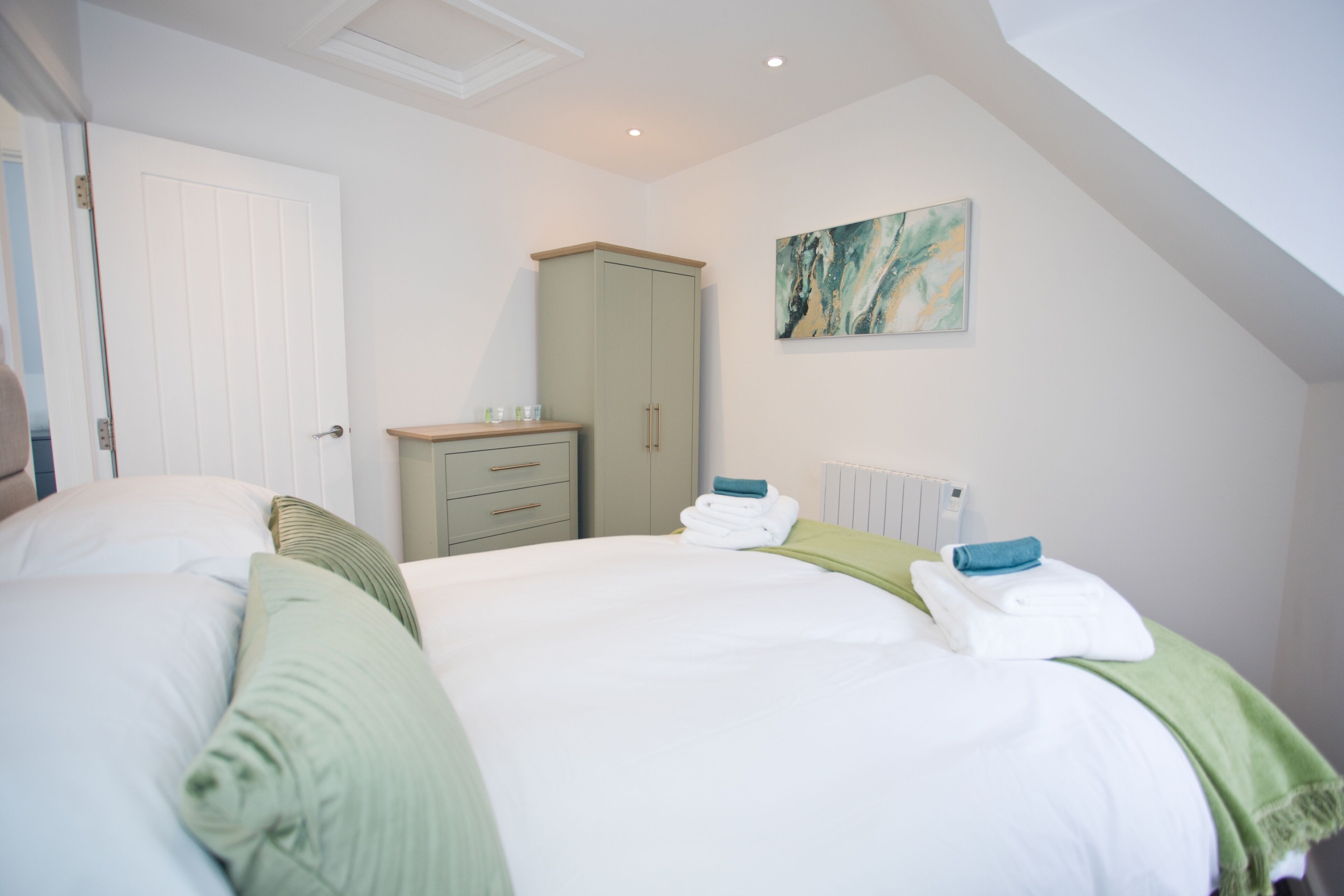 A bedroom with two beds, a wardrobe, a radiator, and a painting on the wall.