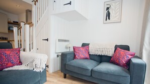 A modern living room with a grey sofa and armchair, a white door, and a staircase.