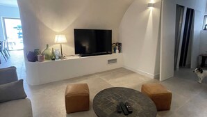 A modern living room with a flat-screen TV, two ottomans, a coffee table, and a sofa. - Air-conditioned 3-bedroom house in quiet location with swimming pool (Junas)