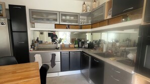 A modern kitchen with stainless steel appliances, a wooden dining table, and black chairs. - Air-conditioned 3-bedroom house in quiet location with swimming pool (Junas)