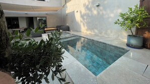 A swimming pool surrounded by a patio area with outdoor furniture, a potted plant, and a building in the background. - Air-conditioned 3-bedroom house in quiet location with swimming pool (Junas)