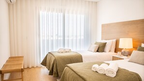 Une chambre d’hôtel avec deux lits, une tête de lit en bois, une table de chevet avec une lampe et un fauteuil en osier.