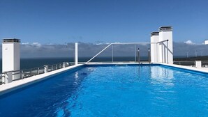 Une piscine offrant une vue dégagée sur l’océan, avec des éoliennes en arrière-plan.