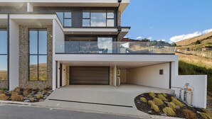 Une maison moderne à deux étages, dotée d’un grand garage, d’un balcon et offrant une vue sur un paysage vallonné.