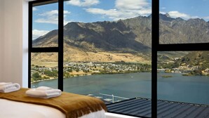 Une chambre d’hôtel dotée d’une grande fenêtre donnant sur un paysage montagneux et un plan d’eau.