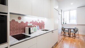 A modern kitchen with white cabinets, a hexagonal backsplash, a built-in oven, and a dining area with a round table and chairs.