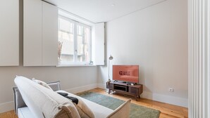 A modern living room with a sofa, a TV on a wooden stand, a window with a view, and a green rug.