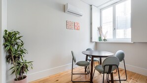 A modern dining area with a round table and four chairs, a potted plant, and a window with a view.