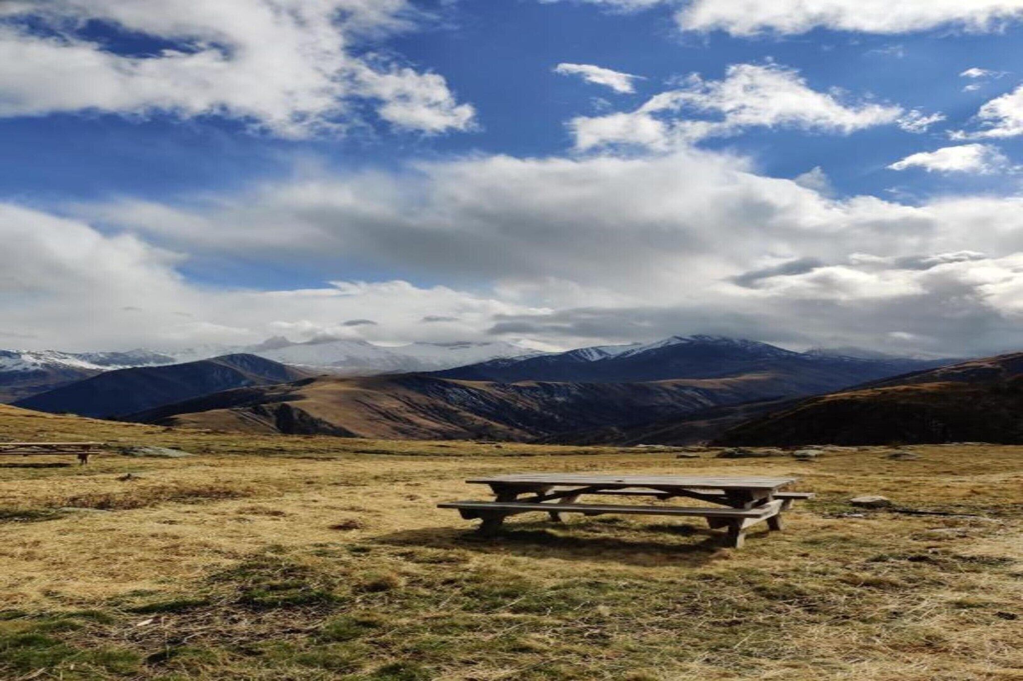 Uma mesa de piquenique em um campo gramado, com montanhas ao fundo.
