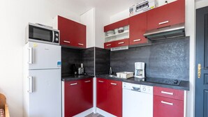 Eine kompakte Küche mit roten und weißen Schränken, einer Mikrowelle, einer Kaffeemaschine und einem Geschirrspüler.
