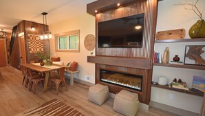 Ein modernes Wohnzimmer mit Kamin, Holzmöbeln und einem flachbildfernseher, der an einer Holzvertäfelung angebracht ist.