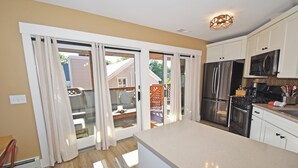 A modern kitchen with white cabinets, stainless steel appliances, and a sliding glass door leading to a patio.