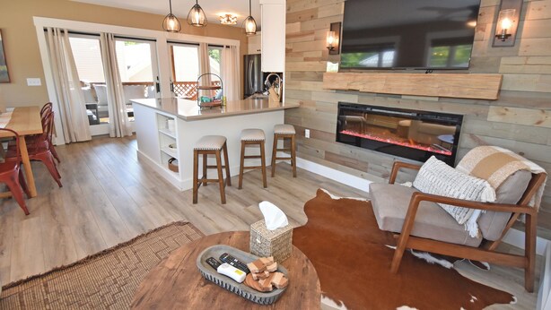 A modern kitchen with a central island, bar stools, a flat-screen TV, and a fireplace.