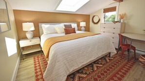 A bedroom with a skylight, a bed with a white and brown bedspread, a desk with a chair, and a dresser.