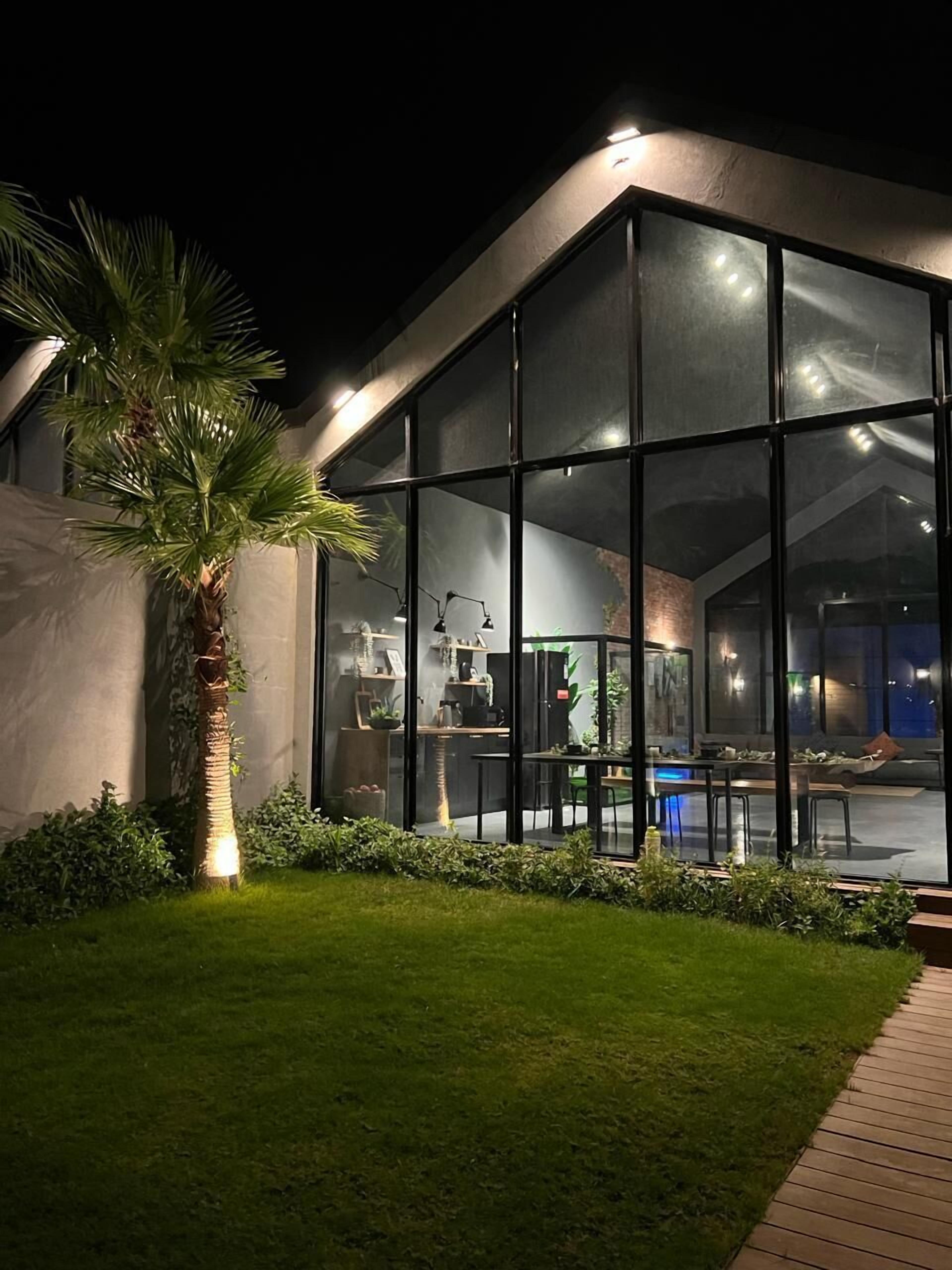 A modern house with large glass windows, a well-maintained lawn, and a palm tree.