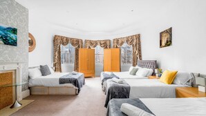Ein Hotelzimmer mit zwei Betten, einer Sitzecke, einem Kamin und großen Fenstern mit Vorhängen.