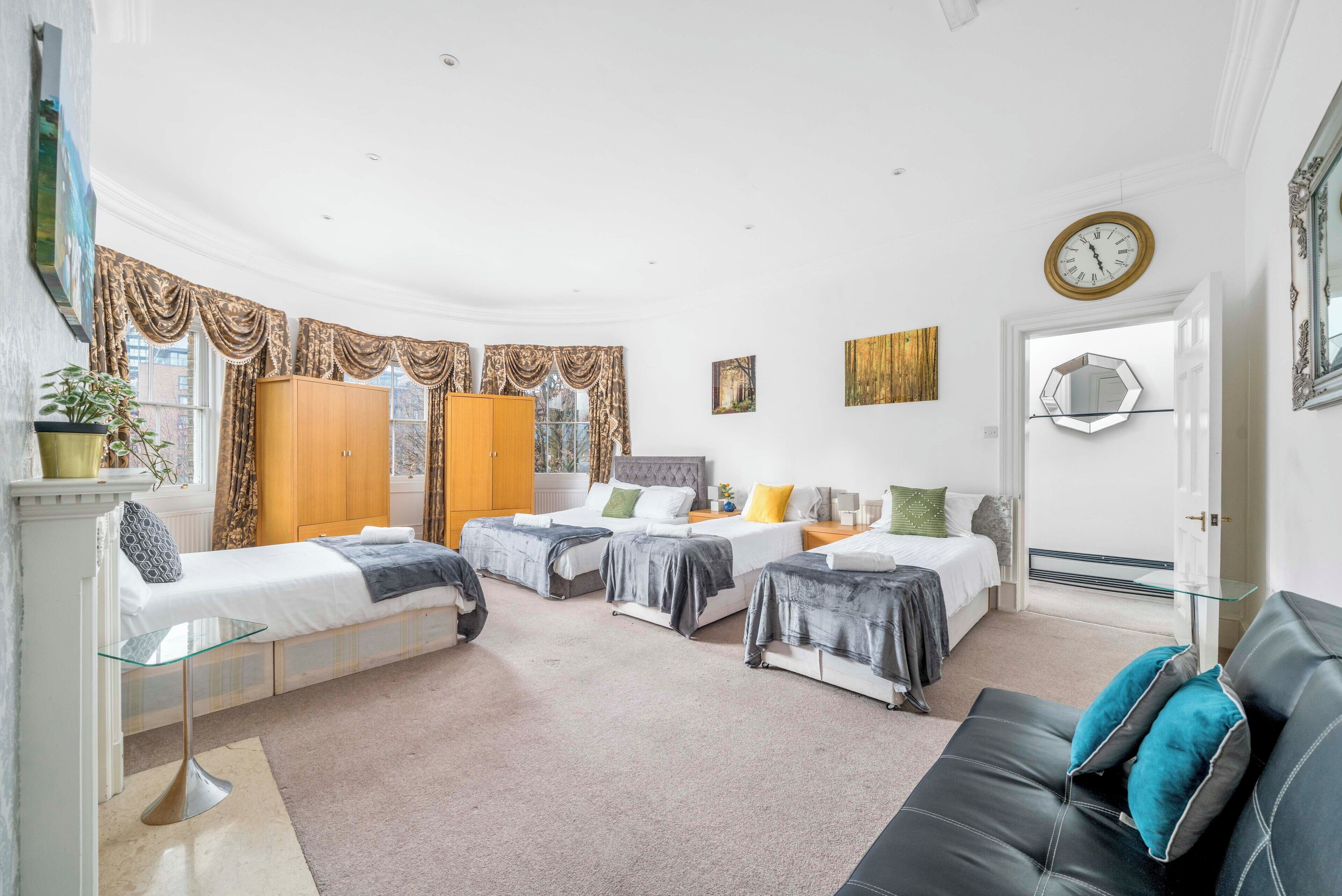 A hotel room with three beds, a black leather sofa, a glass coffee table, and a large mirror on the wall.