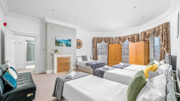 Ein Hotelzimmer mit drei Betten, einem Kamin, einer Couch und einem großen Fenster mit Vorhängen.