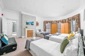 Une chambre d’hôtel avec trois lits, une cheminée, un canapé et une grande fenêtre avec des rideaux.