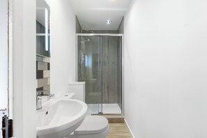 Un baño moderno con ducha de vidrio, lavamanos blanco y espejo.
