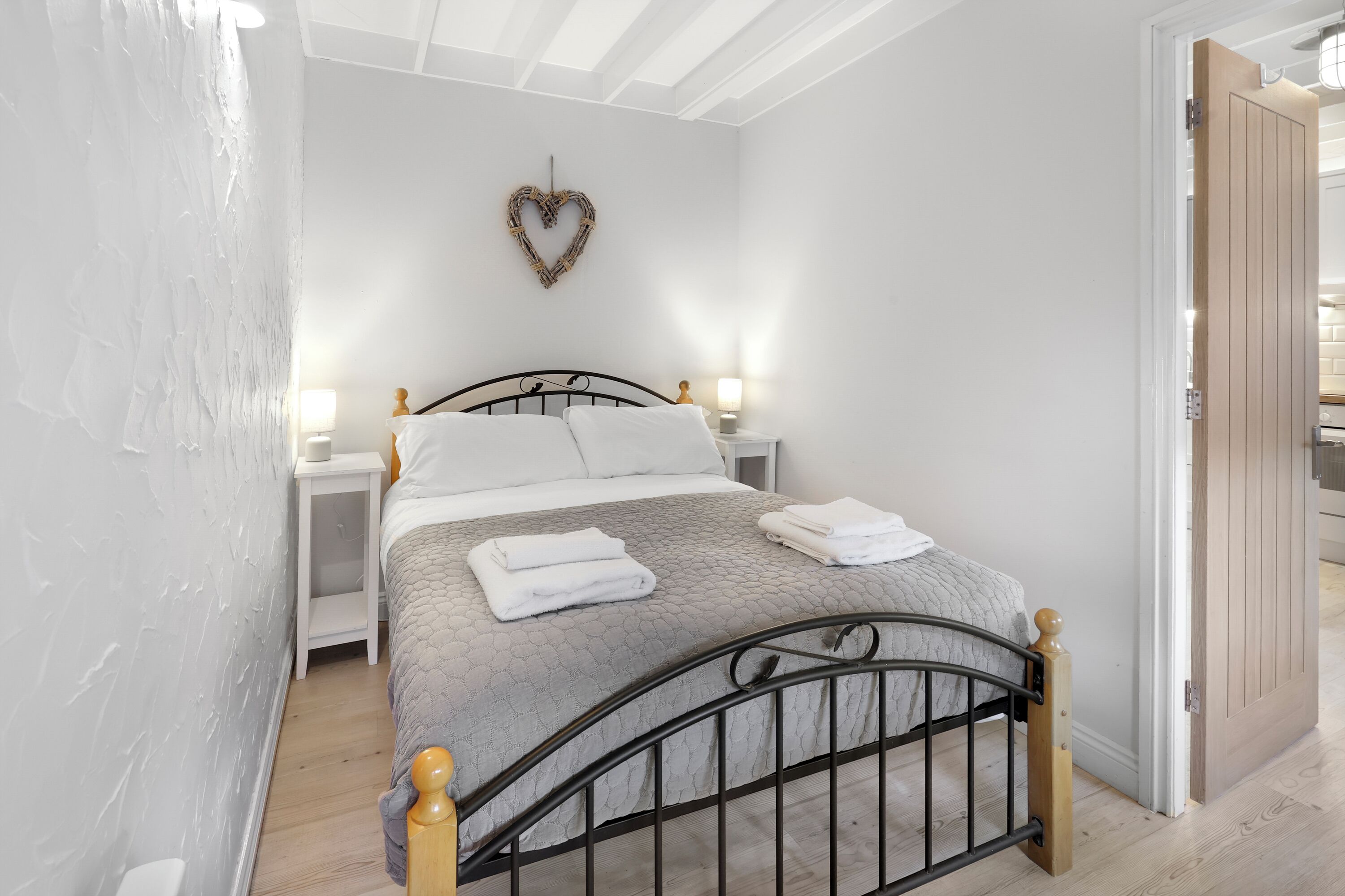 A neatly made bed with white linens, a heart-shaped wall decoration, and bedside lamps.