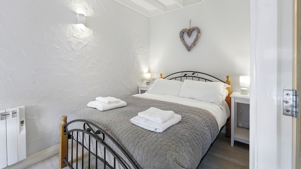 A neatly made bed with folded towels, a heart-shaped decoration on the wall, and a bedside table with a lamp. - Minnow's Rest - North East Escapes (Seahouses)