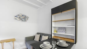 A modern dining area with a black table set for two, a grey sofa with patterned cushions, and a wall-mounted shelf with decorative items. - Minnow's Rest - North East Escapes (Seahouses)