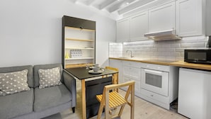 A compact kitchen with white cabinets, a black countertop, and a grey sofa with heart-patterned cushions. - Minnow's Rest - North East Escapes (Seahouses)