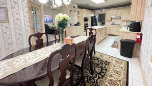 A spacious kitchen with wooden cabinets, a dining table with chairs, a chandelier, and a tiled backsplash. - Charming 3-bedroom house near AT&T Stadium, Six Flag, DFW Airport (Bedford)