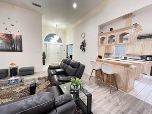 A modern living room with a leather sofa, a glass coffee table, and a view of the kitchen area.