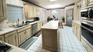 A kitchen with light wooden cabinets, a central island, stainless steel appliances, and a tiled floor. - Charming 3-bedroom house near AT&T Stadium, Six Flag, DFW Airport (Bedford)