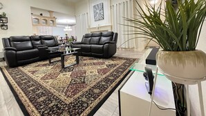 A living room with two black leather sofas, a coffee table, a patterned rug, a ceiling fan, and a potted plant. - Charming 3-bedroom house near AT&T Stadium, Six Flag, DFW Airport (Bedford)