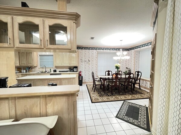 A kitchen with wooden cabinets, a dining table with chairs, a chandelier, and a patterned rug.