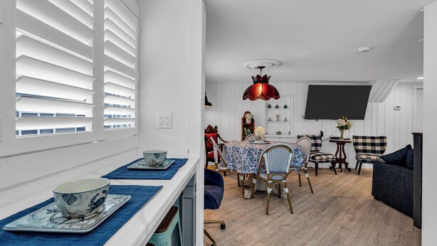 Uma sala de estar moderna com área de jantar, paredes brancas e uma janela grande com persianas.
