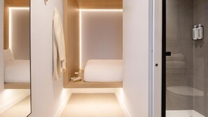 A modern bathroom with a glass shower enclosure, a wooden vanity, and a bedside table with a towel and a book.