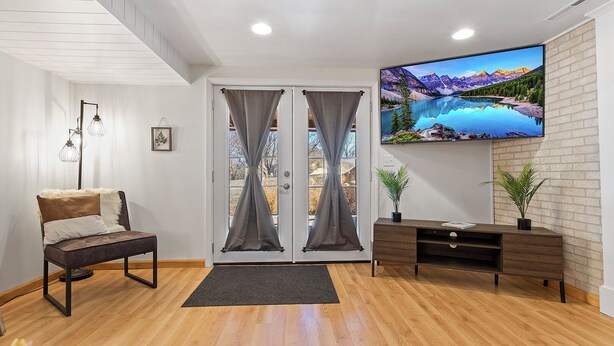 A modern living room with a wooden floor, a sofa with a fur throw, a TV on the wall, and a view of mountains through the curtains. - Spacious 5-bedroom house in welcoming Manhattan (Manhattan)
