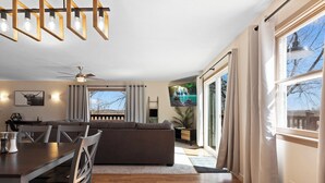A modern living room with a dining area, large windows, and a ceiling fan. - Spacious 5-bedroom house in welcoming Manhattan (Manhattan)