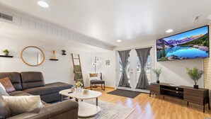 A modern living room with a sofa, coffee table, TV, and a view of mountains through a sliding door. - Spacious 5-bedroom house in welcoming Manhattan (Manhattan)