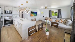Una cocina moderna con electrodomésticos integrados, un comedor con mesa y sillas de madera, y una sala de estar con sofá y un ventanal grande.