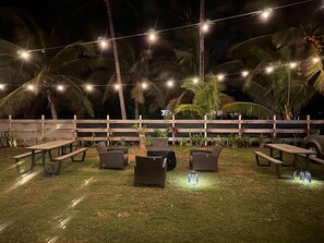 Un espace extérieur aménagé avec des tables et des chaises, des guirlandes lumineuses et des palmiers.