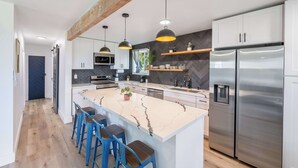 A modern kitchen with a central island, bar stools, stainless steel appliances, and pendant lighting. - Oahu Oceanfront Getaway (Hauula)