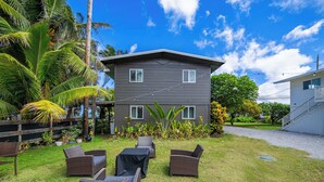 A two-story building with a flat roof, surrounded by a grassy lawn and various tropical plants. - Oahu Oceanfront Getaway (Hauula)