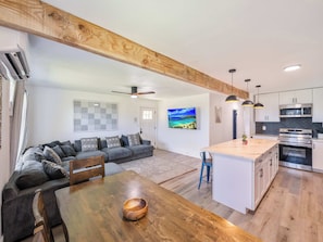 A modern kitchen with white cabinets, a wooden island, and a dining area with a wooden table. - Oahu Oceanfront Getaway (Hauula)